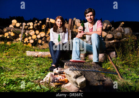 Tyrol - Young couple sitting on alpine meadow of a mountain on Campfire in the Bavarian Alps and enjoys the romantic evening Stock Photo