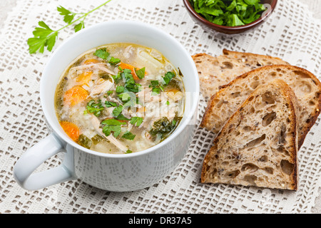 Cup of hot chicken rice soup served with bread and parsley on crochet tablecloth Stock Photo