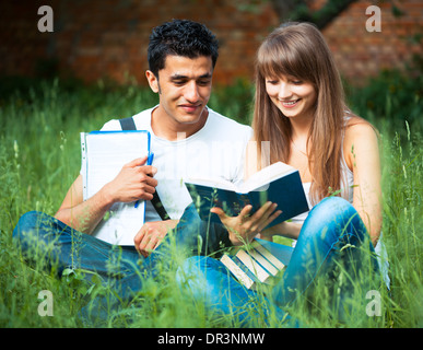 Two students guy and girl studying in park on grass with book outdoors Stock Photo