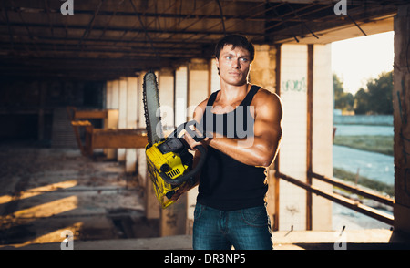 Muscular man with a chainsaw on the ruins Stock Photo