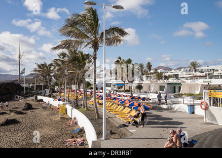 Typical white holiday apartments on waterfront lined with sunbeds overlooking Playa Chica beach in Puerto del Carmen Lanzarote Stock Photo