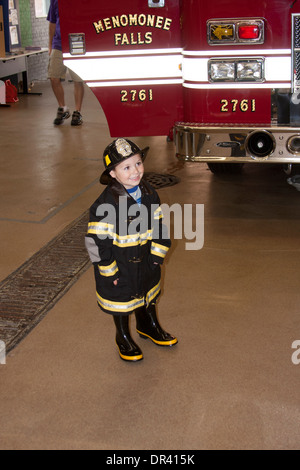 A little girl posing in a firefighter uniform in front of the Menomonee Falls Fire Engine WI Stock Photo