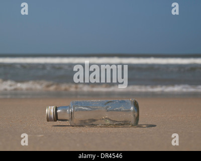 Empty bottle in the sand in front of the sea Stock Photo