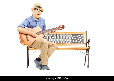 Ecstatic young guitarist sitting on bench and singing Stock Photo