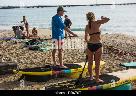 A man and women practice using stand-up paddle boards before taking them out on the water in St. Croix, U.S. Virgin Islands Stock Photo