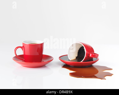 Two red espresso coffee cups, one cup with spilled coffee isolated on white background Stock Photo