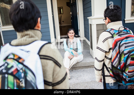 Hispanic mother greeting sons at door Stock Photo