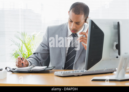 Businessman using computer and phone at office desk Stock Photo
