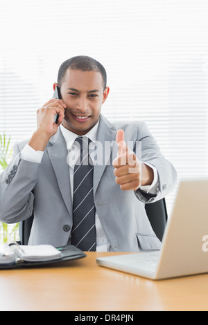 Smiling businessman gesturing thumbs up while on call Stock Photo