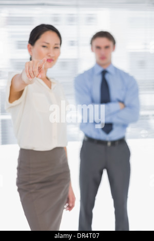 Businesswoman pointing towards camera with man in office Stock Photo