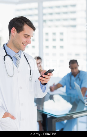 Doctor text messaging with group around table in hospital Stock Photo
