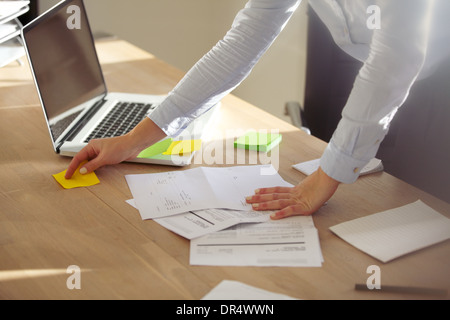 Closeup of businesswoman checking notes on sticky note. Female executive in office with sticky notes and laptop with documents Stock Photo
