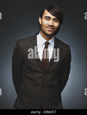 Portrait of charming young businessman looking at camera smiling. Well dressed asian male model posing against black background Stock Photo