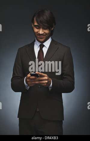 Happy young executive texting on his smart phone. Handsome male associate reading test message on his cell phone. Stock Photo