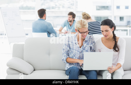 Women using laptop with colleagues in background at creative office Stock Photo