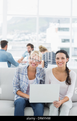 Women using laptop with colleagues in background at creative office Stock Photo