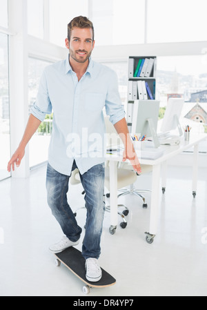 Happy young man skateboarding in creative office Stock Photo