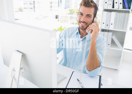 Smiling man using phone and computer in office Stock Photo