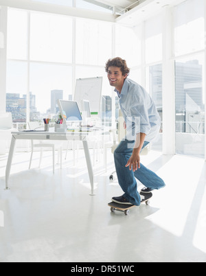 Happy man skateboarding in a bright office Stock Photo