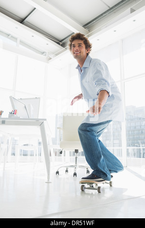 Happy young man skateboarding in office Stock Photo