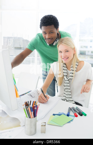 Artist drawing something on paper while using computer with colleague Stock Photo