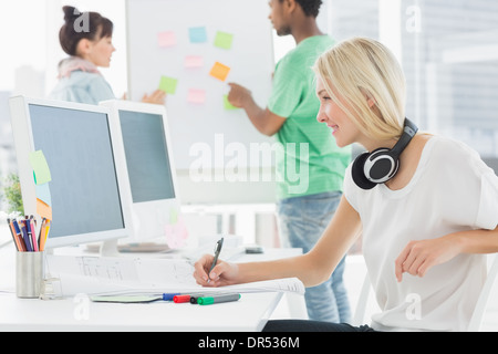 Artist drawing something on paper with colleagues behind at office Stock Photo