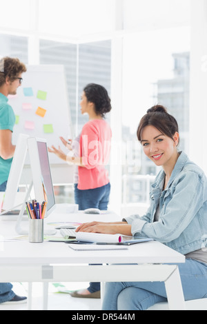 Casual woman using computer with colleagues behind in office Stock Photo