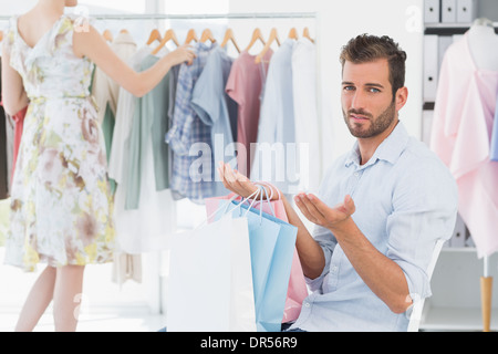 Bored man with shopping bags while woman by clothes rack Stock Photo