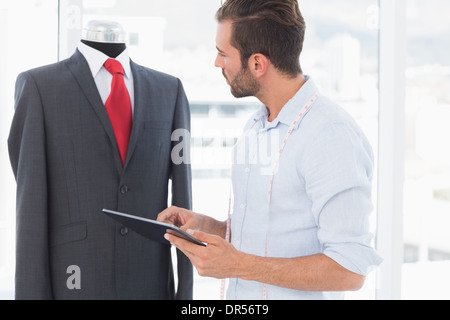 Concentrated fashion designer with digital tablet looking at suit on dummy Stock Photo