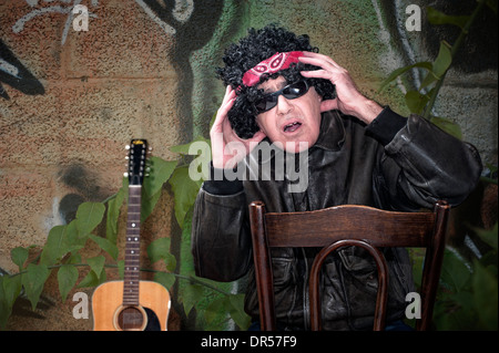Stressed out rocker middle age man with bandana sitting on chair Stock Photo