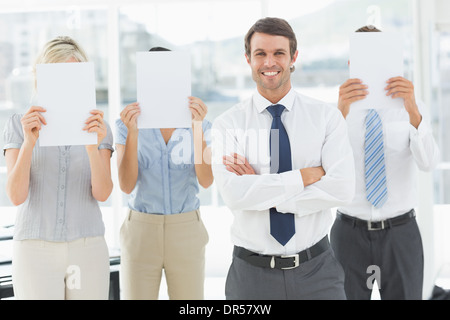 Businessman with colleagues holding blank paper in front of faces Stock Photo