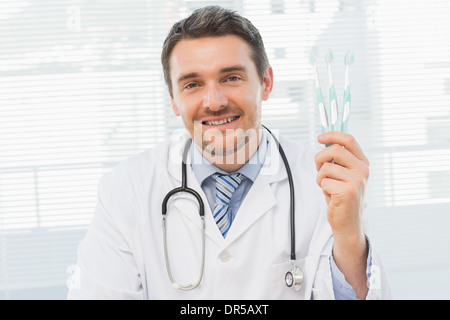 Smiling doctor holding toothbrushes in office Stock Photo