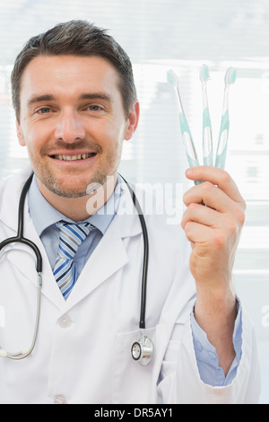 Smiling doctor holding toothbrushes in office Stock Photo