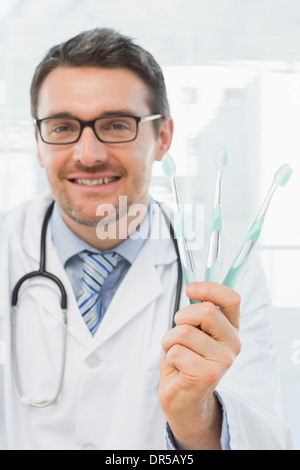 Smiling doctor holding toothbrushes in office Stock Photo