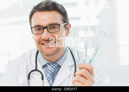 Smiling doctor holding toothbrushes in office Stock Photo