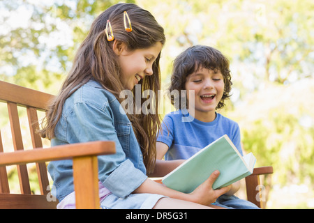 Side view of kids reading book on park bench Stock Photo