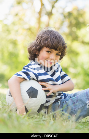 Cute little boy with football sitting on grass in park Stock Photo