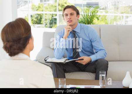 Young businessman listening to colleague sitting on couch Stock Photo