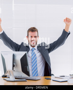 Cheerful businessman clenching fist at office desk Stock Photo