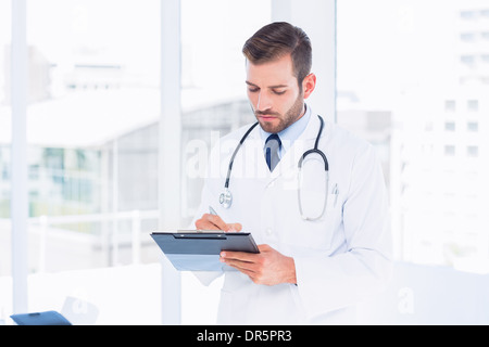 Concentrated male doctor writing reports in clipboard Stock Photo