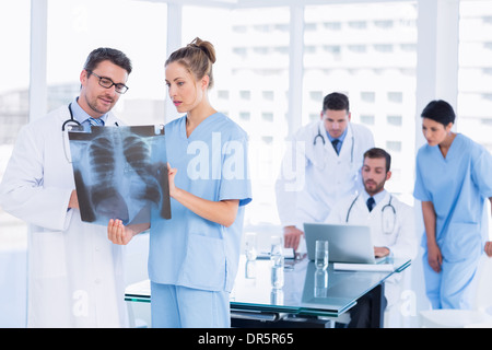 Doctors examining x-ray with colleagues using laptop behind Stock Photo