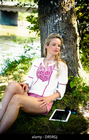 Young woman leaning against tree, eyes closed, foothills of the Alps, Bavaria, Germany Stock Photo