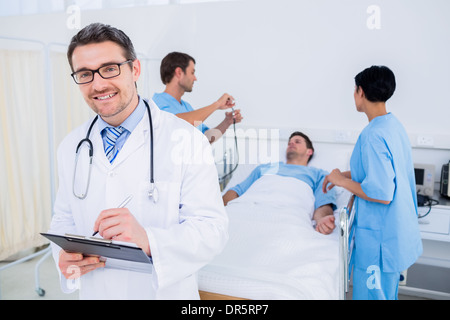 Doctor writing reports with patient and surgeons in background Stock Photo