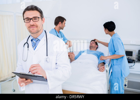 Doctor writing reports with patient and surgeons in background Stock Photo