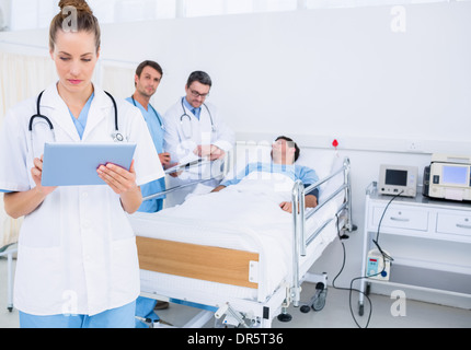 Doctor using digital tablet with colleagues and patient behind Stock Photo