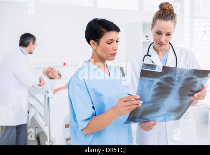 Doctors examining x-ray with patient in background Stock Photo