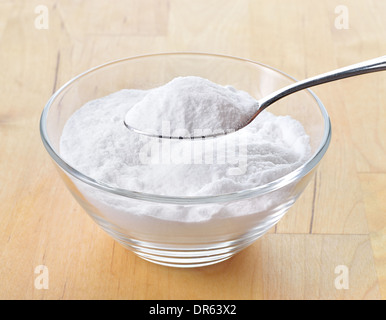 Close-up of baking soda on spoon against background of glass of water on wooden table. Bicarbonate of soda. Stock Photo