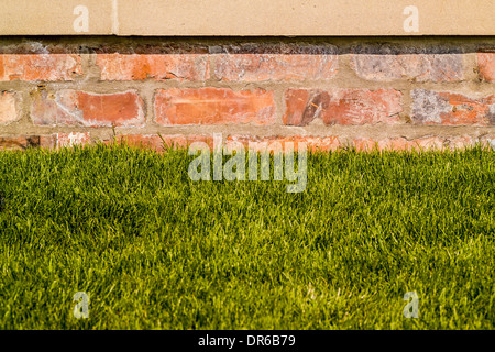 Brick garden wall with sandstone coping stone on top and lawn at bottom Stock Photo
