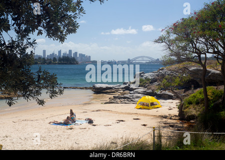 Milk Beach with people relaxing Sydney Harbour Bridge and city skyline in background Sydney New South Wales NSW Australia Stock Photo