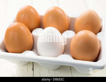Half dozen brown eggs with one white in ceramic white container Stock Photo